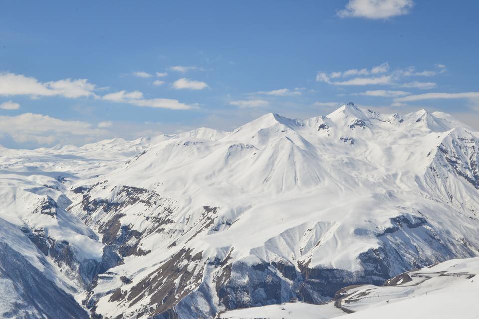 Snow-covered ridges and peaks of the Greater Caucasus above Gudauri, Georgia, in winter sunshine under a blue sky with a few white clouds