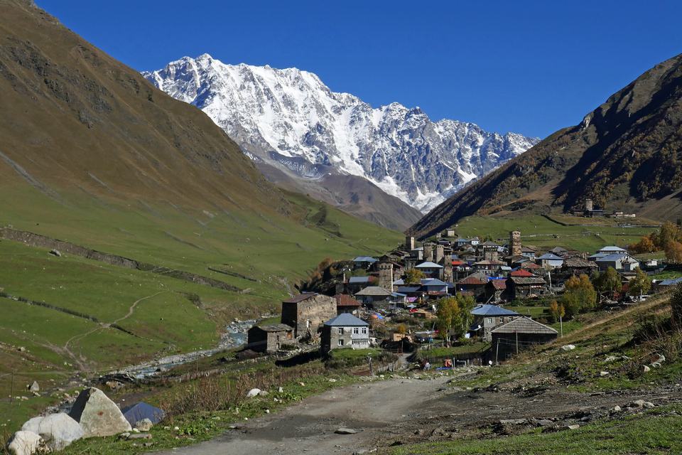 格鲁吉亚上斯瓦涅季的乌树故里村:秋天的山谷里是中世纪石砌塔楼和石板屋顶的村舍,背后是积雪的什哈拉峰,天空湛蓝无云